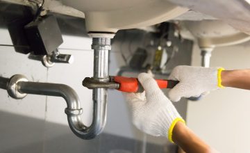 Plumber fixing white sink pipe with adjustable wrench.