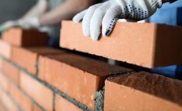 Two workers making red brick wall at construction site close-up